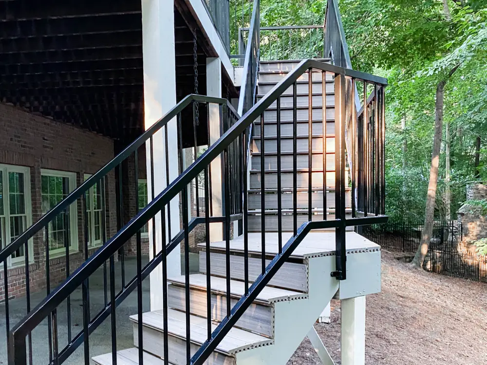 A new deck with black metal railings and composite stairs beside a brick home, with a screened porch above.