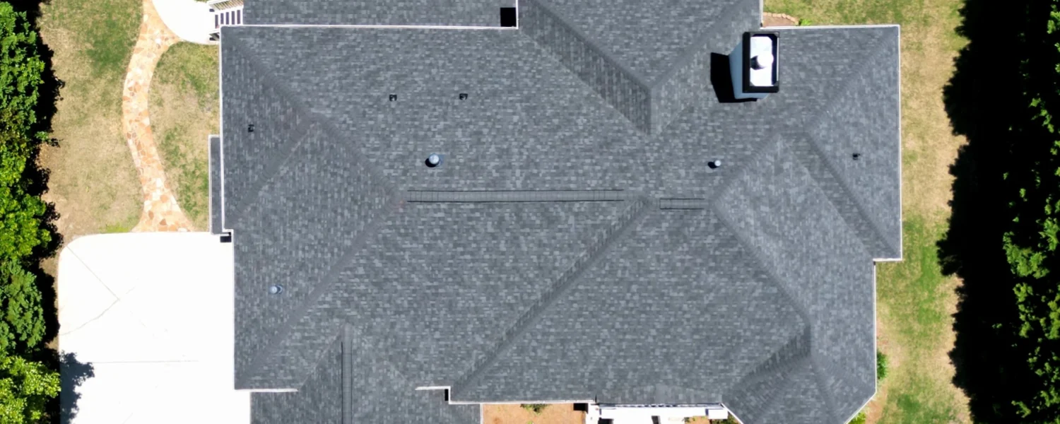 Overhead view of a finished grey shingle roof and the driveway beside it.
